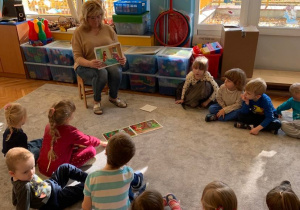 Biblioterapia w grupie 1. Dzieci siedzą na dywanie, Nauczycielka pokazuje ilustrację.